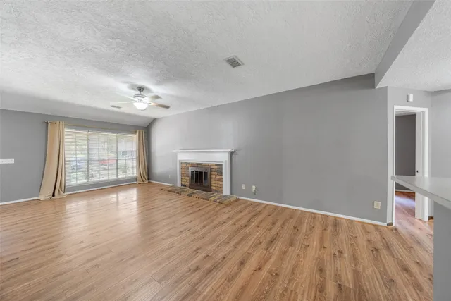 an empty room with wooden floor fireplace and windows