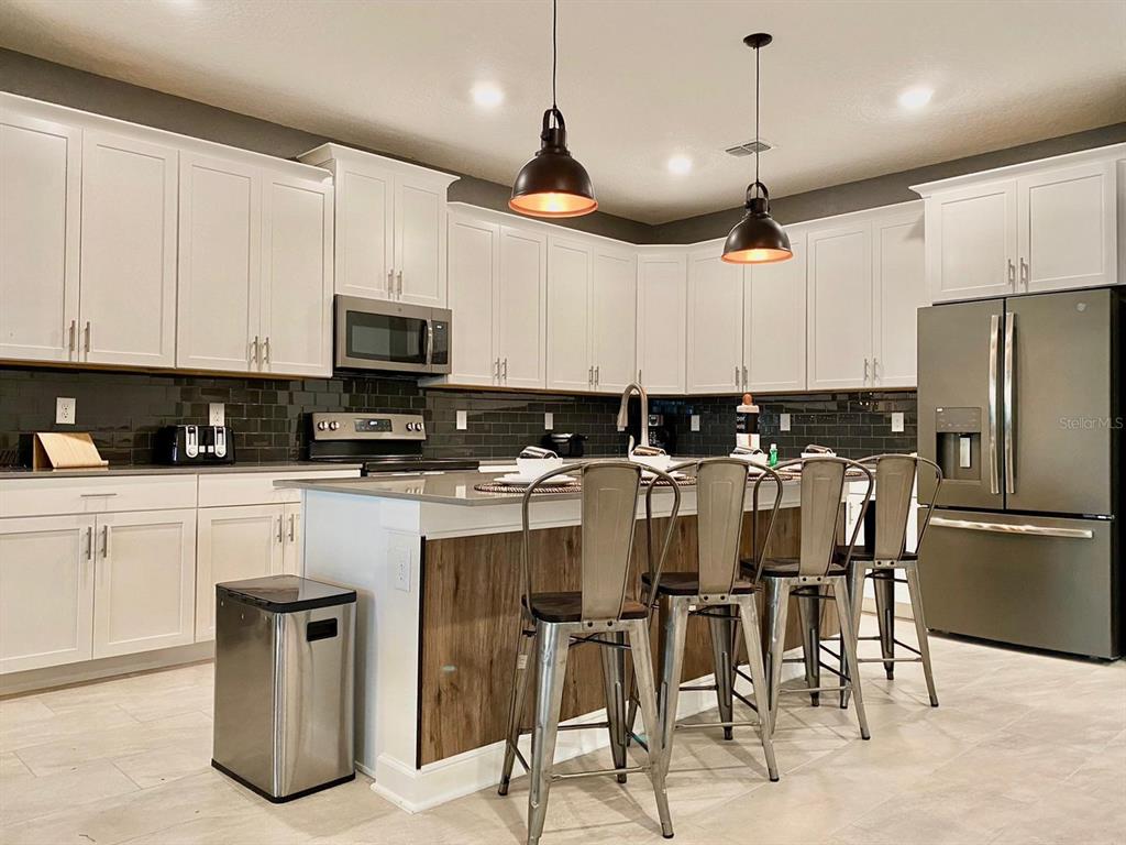 8983 Backswing Way Davenport, FL 33896 - Photo 3 of 30 a kitchen with stainless steel appliances granite countertop a sink a stove a refrigerator cabinets and chairs