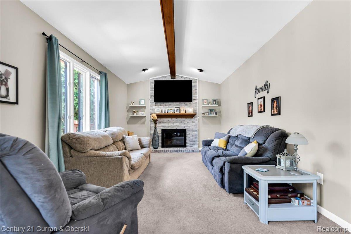 21439 Hall Road Trenton, MI 48183 - Photo 13 of 35 Living area featuring a vaulted ceiling with exposed wood beams, a stone-clad fireplace, and large picture windows