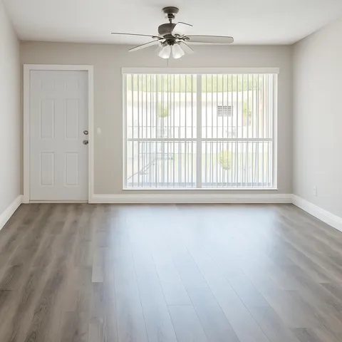 an empty room with wooden floor fan and windows