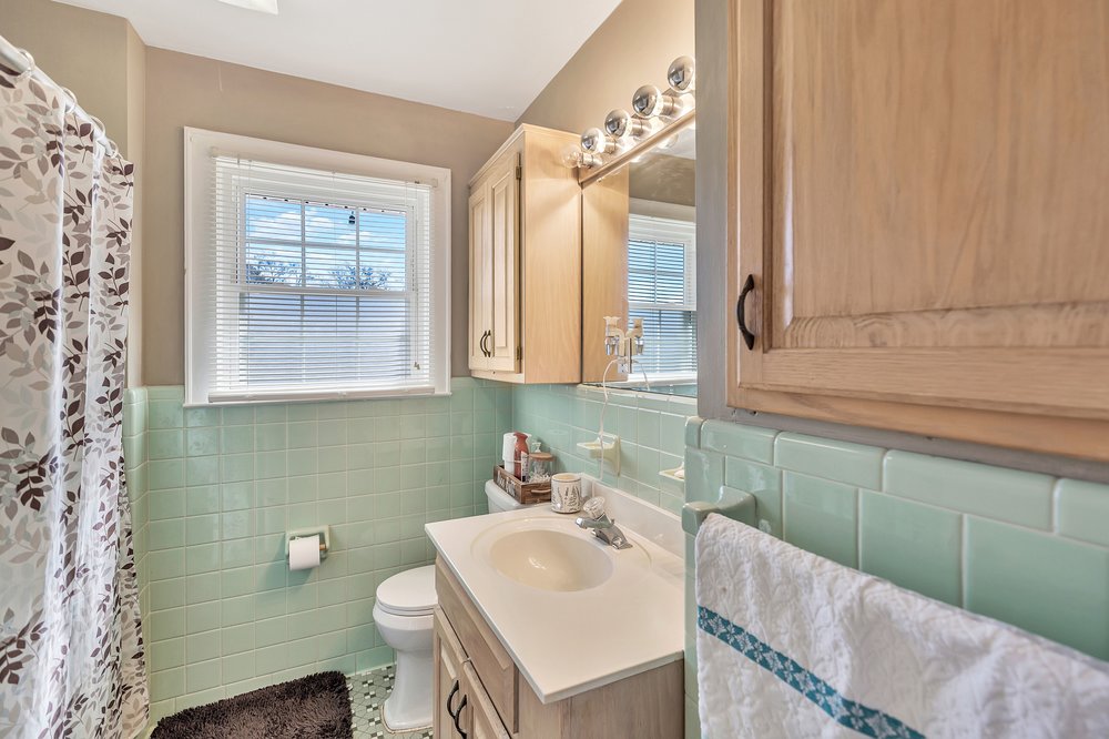 105 West Church Street Iva, SC 29655 - Photo 14 of 25 This bathroom features light green wall tiles and a vanity with a mirror, creating a functional space.