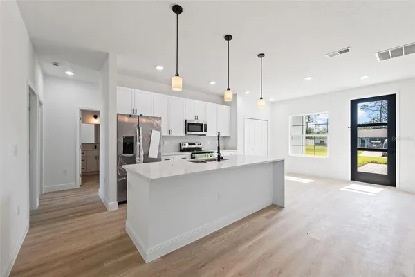 a large kitchen with kitchen island a stove a refrigerator a sink a dining table and chairs with wooden floor