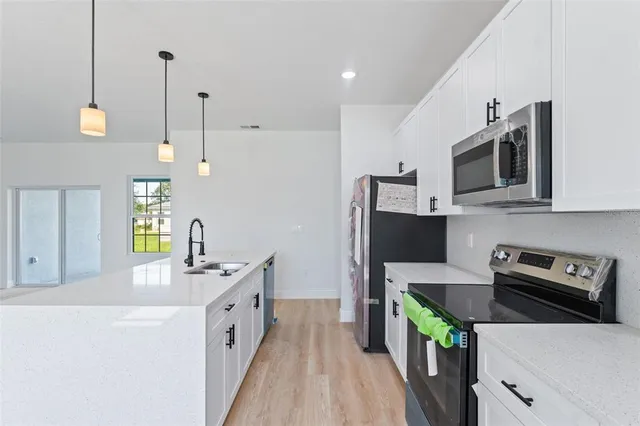 a kitchen with stainless steel appliances a stove a sink a microwave a refrigerator white cabinets and wooden floor