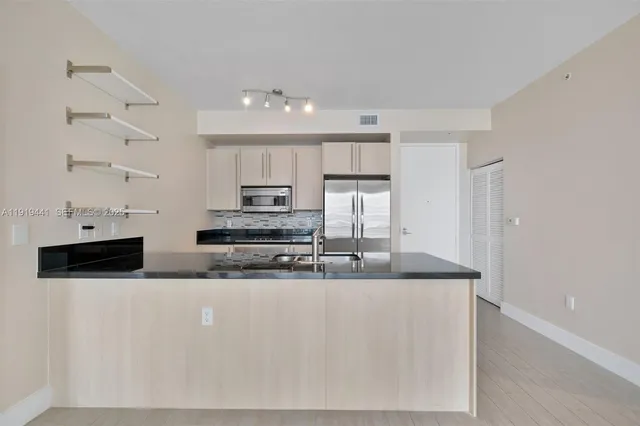 a large kitchen with stainless steel appliances a sink a stove a microwave and white cabinets