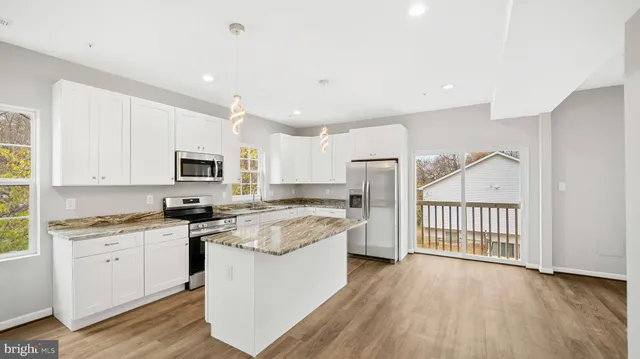 a kitchen with stainless steel appliances granite countertop a stove top oven a sink a refrigerator and white cabinets with wooden floor