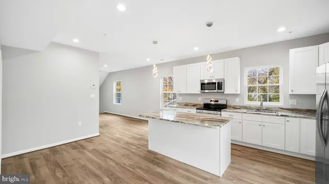 a kitchen with stainless steel appliances granite countertop a stove top oven a sink a refrigerator and white cabinets with wooden floor