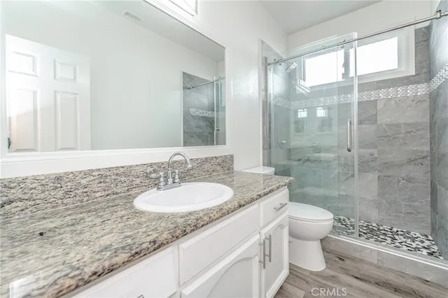 a bathroom with a granite countertop sink a toilet a mirror and shower