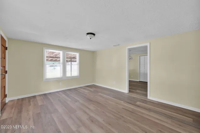 a view of an empty room with wooden floor and a window