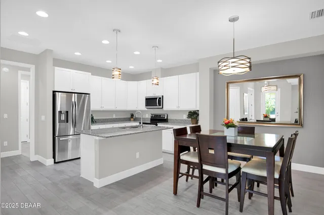 a kitchen with stainless steel appliances kitchen island granite countertop a dining table chairs refrigerator and cabinets