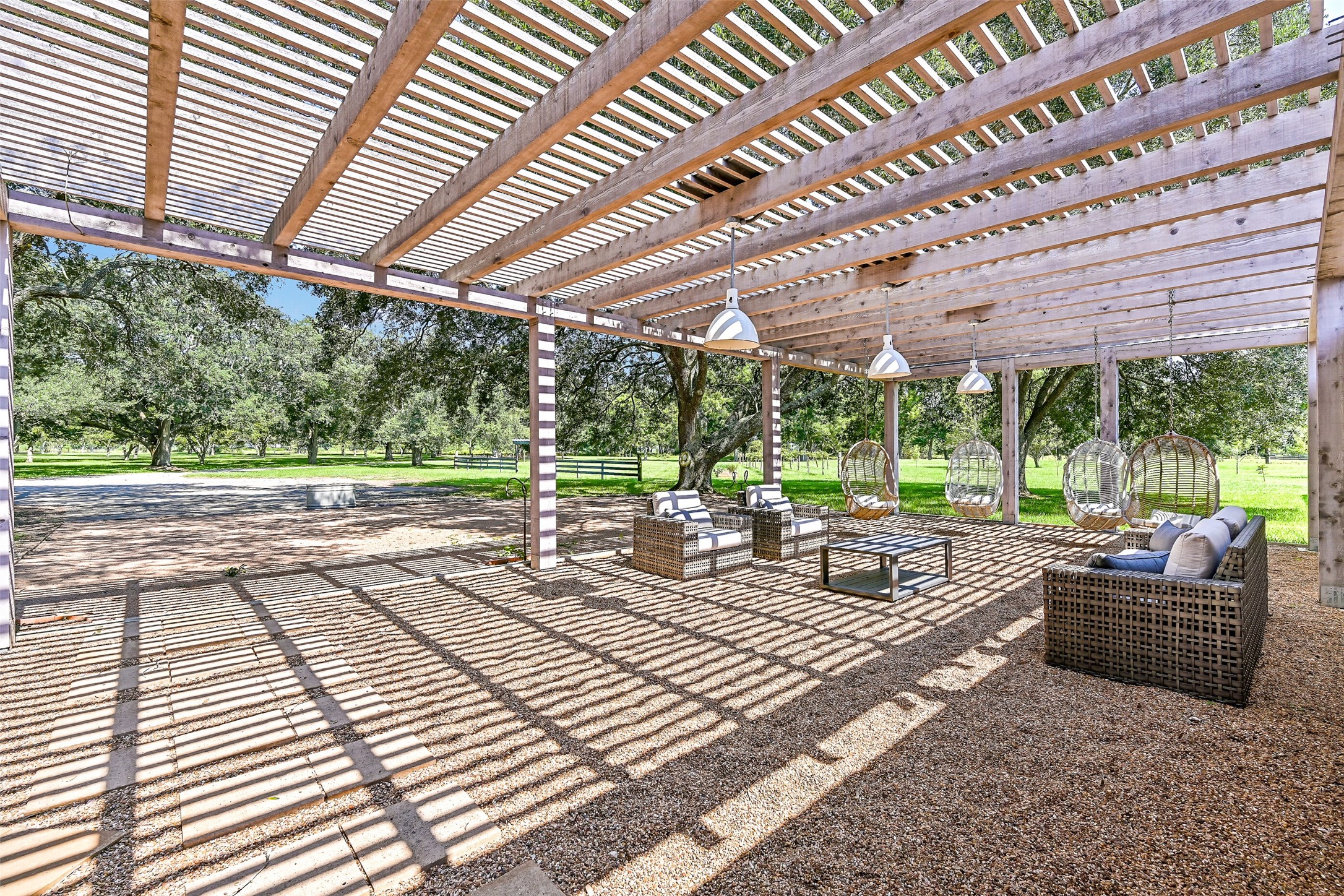 3042 Poskey Road Anahuac, TX 77514 - Photo 40 of 50 Discover a chic outdoor oasis with a pergola, featuring hanging chairs and cozy wicker seating—ideal for relaxing or entertaining amidst tranquil greenery.