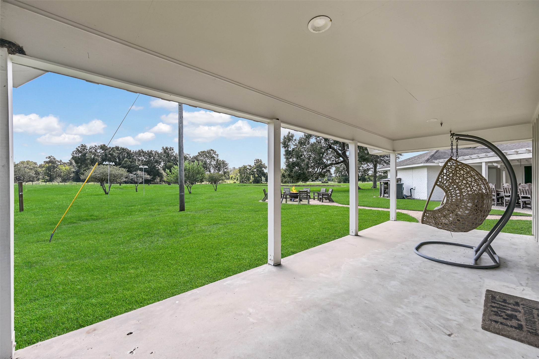 3042 Poskey Road Anahuac, TX 77514 - Photo 41 of 50 Experience tranquility on this covered patio off the primary suite, featuring a hanging chair and scenic views of a lush lawn and peaceful trees—perfect for relaxation and gatherings.