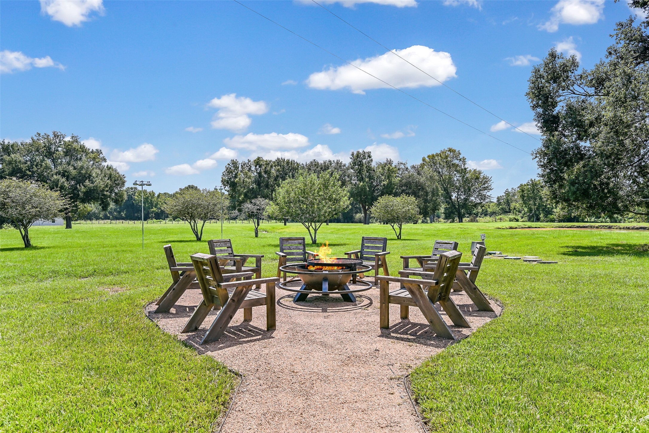 3042 Poskey Road Anahuac, TX 77514 - Photo 43 of 50 Discover serenity in this expansive backyard, complete with a cozy fire pit and wooden seating, surrounded by mature trees—perfect for relaxing and entertaining.