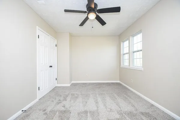 an empty room with chandelier fan and windows