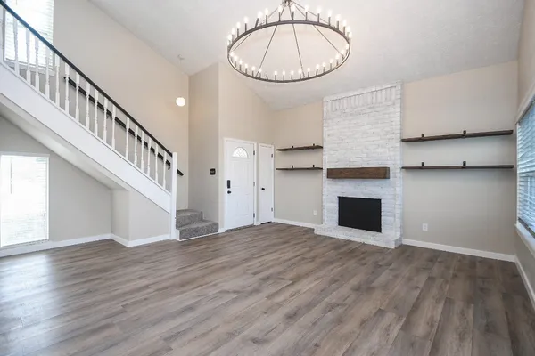 a view of an empty room with wooden floor and a kitchen