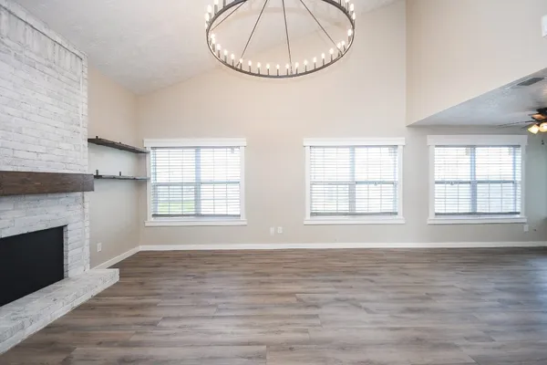 an empty room with wooden floor fireplace and windows