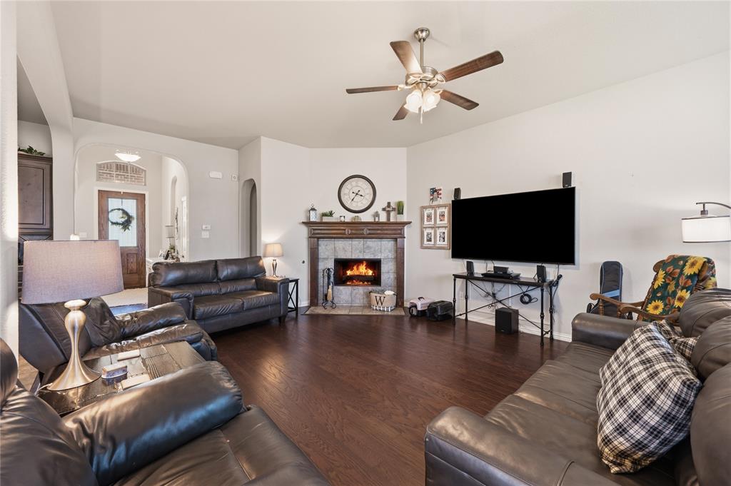 140 Chestnut Road Waxahachie, TX 75165 - Photo 8 of 26 Spacious living area featuring wood-finish flooring, a corner fireplace with a tiled surround and wood mantel, and a ceiling fan with integrated lighting