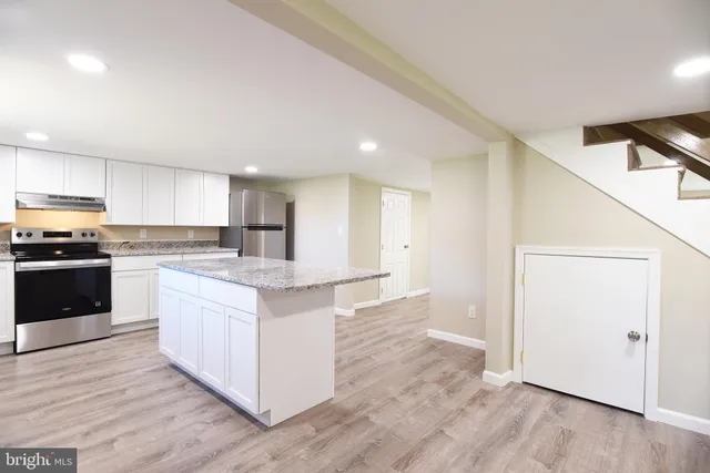 a large kitchen with granite countertop a stove top oven a sink and white cabinets with wooden floor