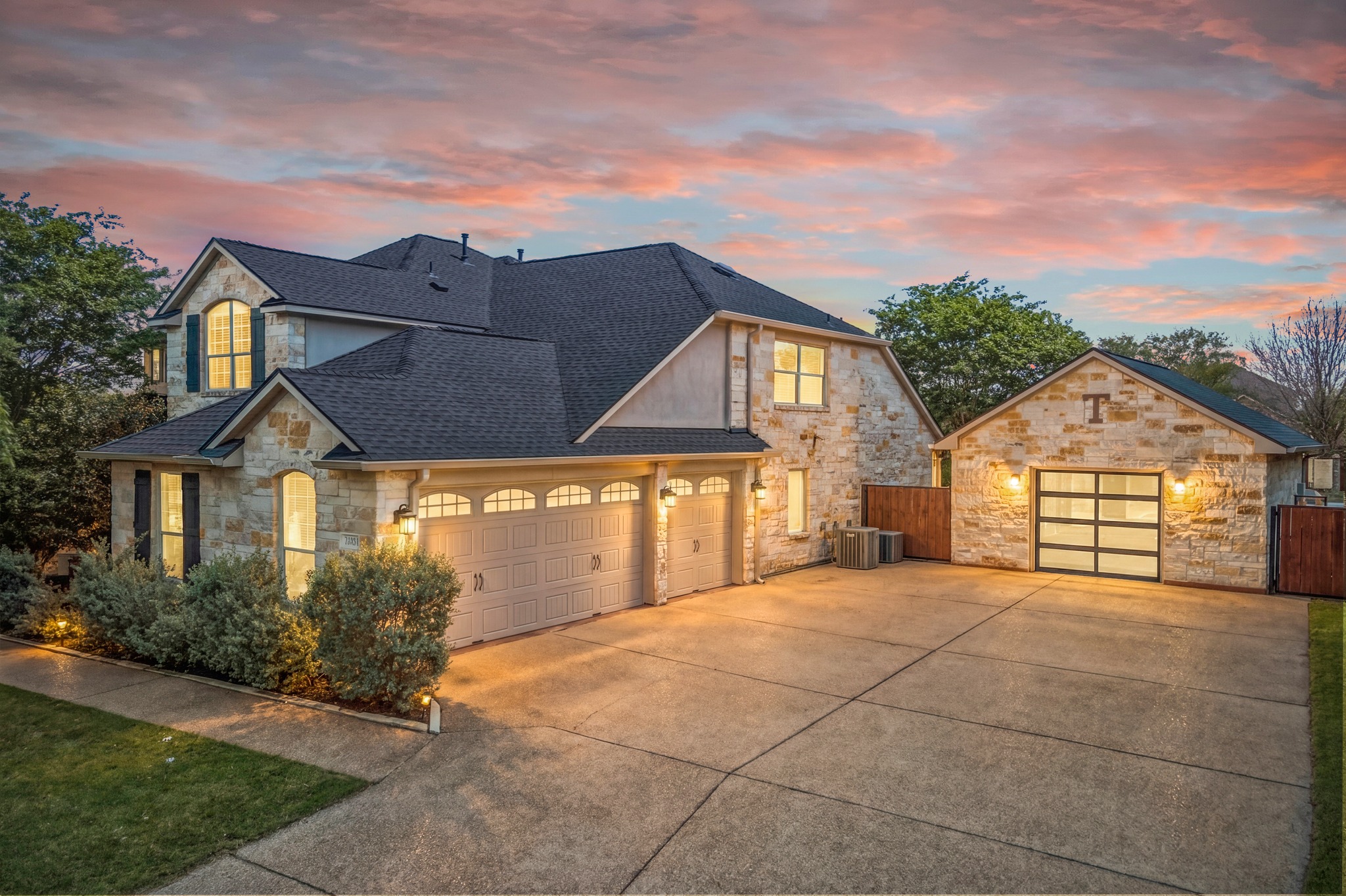 Stone facade residence featuring a multi-car driveway, 3 car attached garage with carriage-style doors, and a detached stone fully finished garage with a modern glass-panel door.