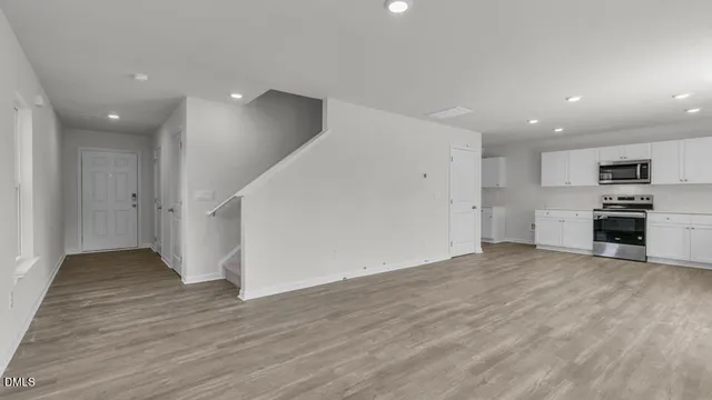 an empty room with wooden floor and kitchen view