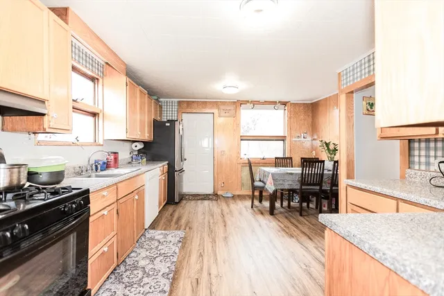 a kitchen with stainless steel appliances granite countertop a stove top oven a sink a dining table and chairs with wooden floor