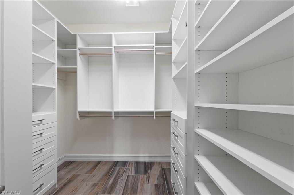 9076 Rialto Street, Unit 6204 Naples, FL 34113 - Photo 20 of 50 Custom closet system featuring white cabinetry, varied shelving, integrated drawers with brushed nickel hardware, hanging rods, and wood-finish flooring. NEW INSPIRED CLOSETS CUSTOM CLOSET ORGANIZERS (2018), NEW TILE FLOOR (2018)