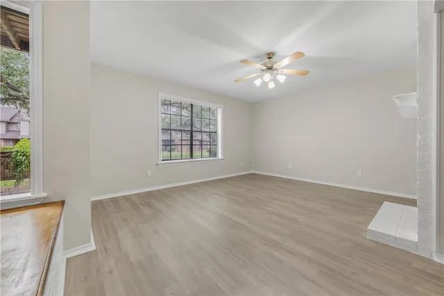 an empty room with wooden floor fan and windows