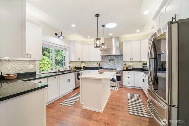 a kitchen with stainless steel appliances granite countertop a refrigerator a sink dishwasher a stove and white countertops with wooden floor