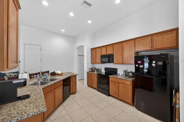 a kitchen with stainless steel appliances granite countertop a stove top oven a sink dishwasher a refrigerator and a dining table with wooden floor