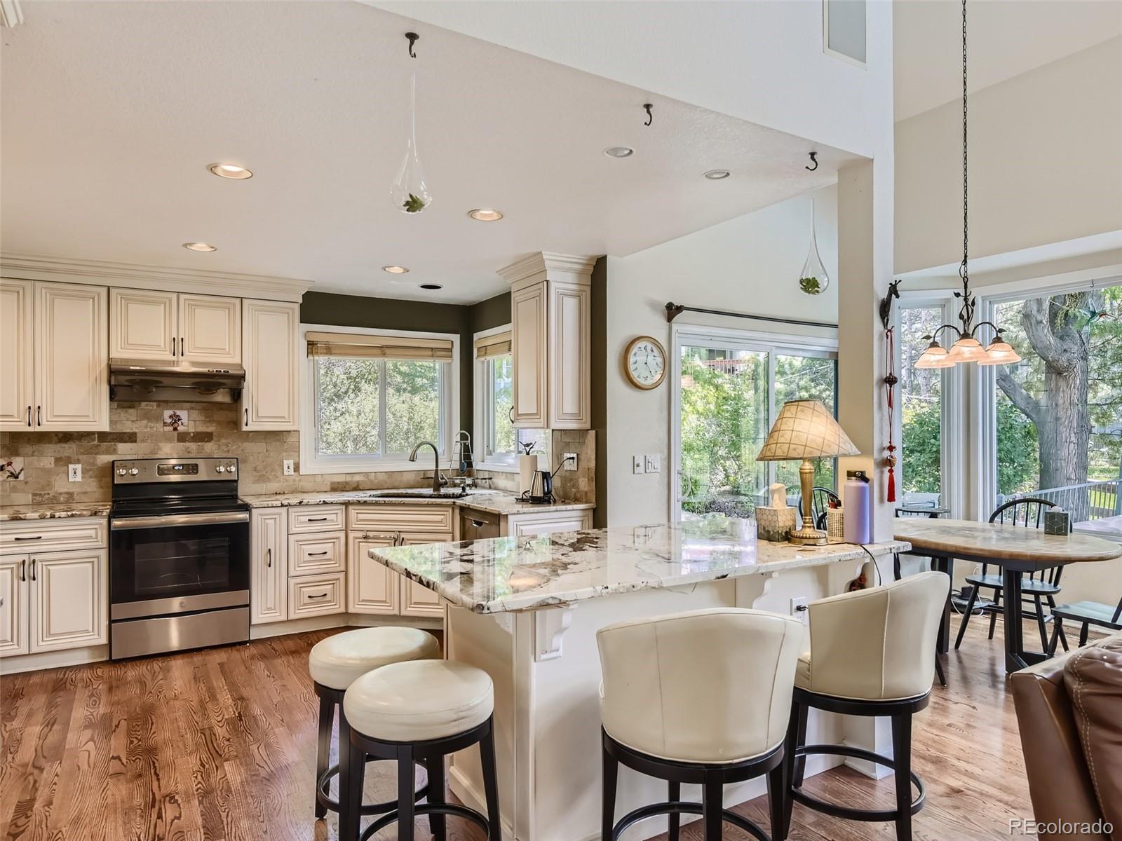 6722 Eagle Place Highlands Ranch, CO 80130 - Photo 5 of 34 a kitchen with stainless steel appliances granite countertop a stove a refrigerator a kitchen island a dining table and chairs with wooden floor