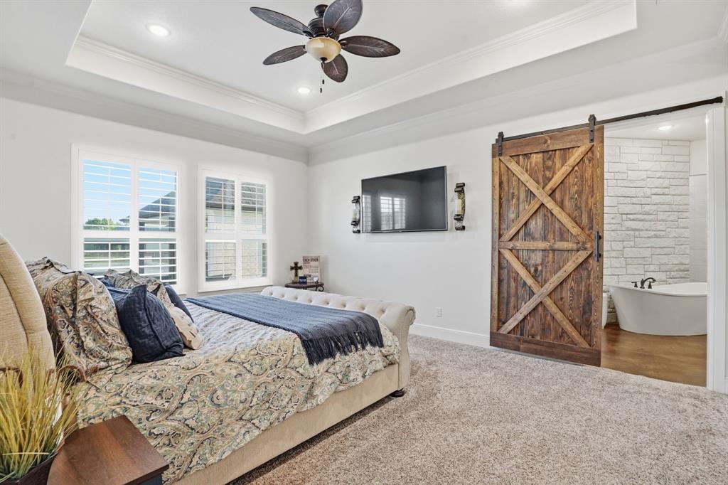 103 Apollo Trail Aurora, TX 76078 - Photo 27 of 40 Carpeted bedroom with a barn door, connected bathroom, a ceiling fan, crown molding, and a tray ceiling
