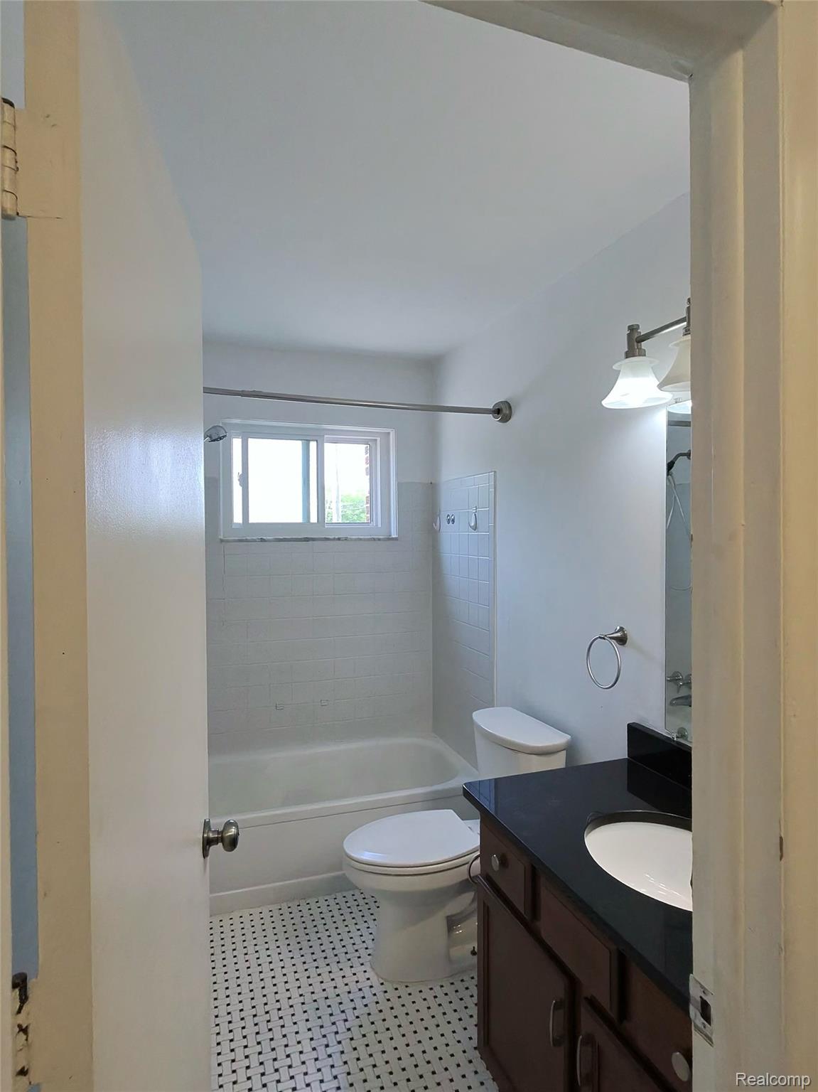 25301 Five Mile Road, Unit 130 Redford, MI 48239 - Photo 8 of 15 Bathroom featuring a bathtub with subway tile surround, a single vanity with a dark countertop and undermount sink, and black and white mosaic tile flooring