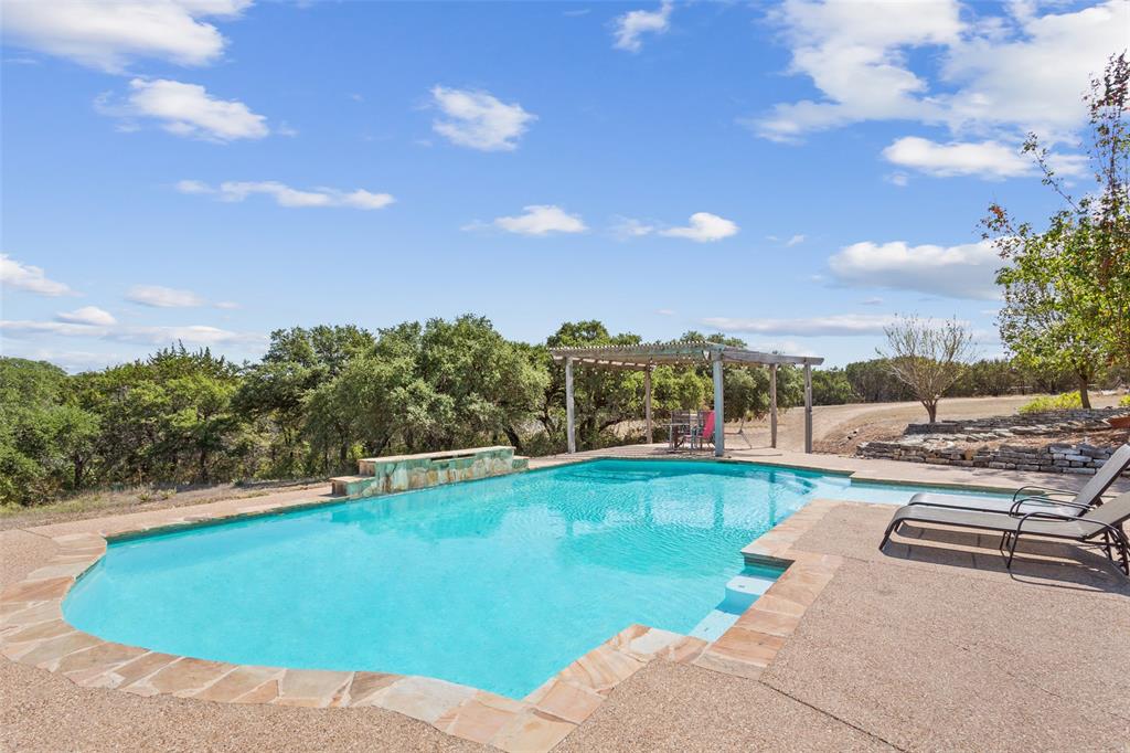 564 Sam Bass Road McGregor, TX 76657 - Photo 26 of 37 Expansive outdoor pool area featuring a freeform swimming pool with a stone coping, a built-in waterfall feature, and a pergolated patio space