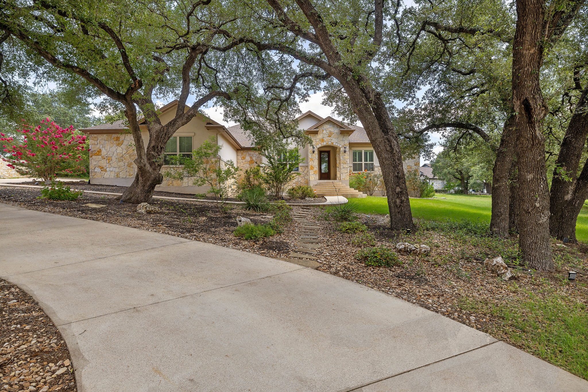 231 Marbella Way Georgetown, TX 78633 - Photo 34 of 40 Mature trees frame a charming home with a stone and stucco facade, featuring a well-maintained lawn and paved driveway.