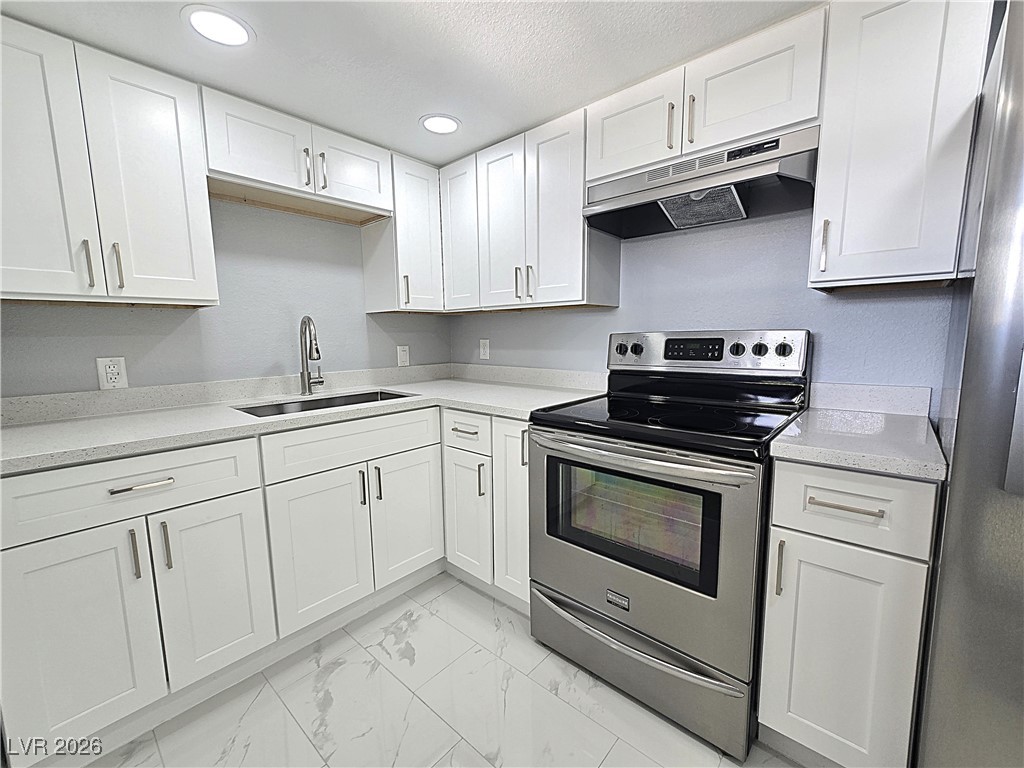 Kitchen with stainless steel range with electric cooktop, under cabinet range hood, white cabinets, light marble finish floors, and a textured ceiling