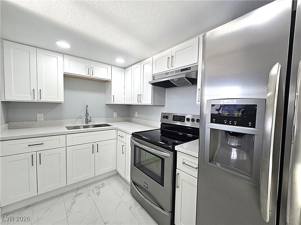 1437 Chestnut Street Henderson, NV 89011 - Photo 2 of 23 Kitchen with appliances with stainless steel finishes, light marble finish floors, white cabinets, under cabinet range hood, and a textured ceiling