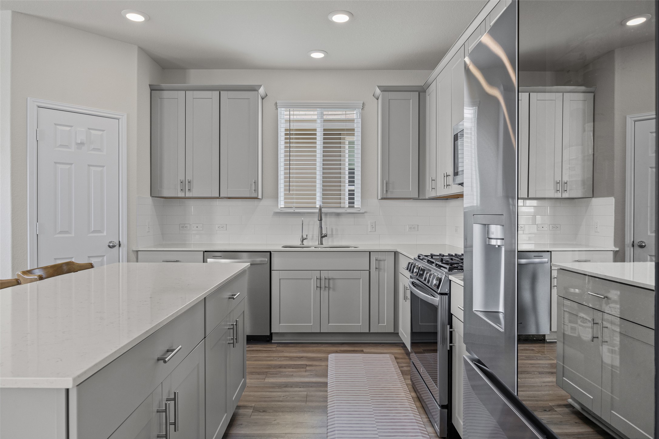 208 Orange Road Buda, TX 78610 - Photo 5 of 31 A chef's kitchen showcasing contemporary grey cabinetry, white countertops, and stainless steel appliances.