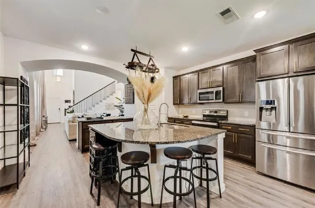 a kitchen with stainless steel appliances a dining table chairs refrigerator and microwave
