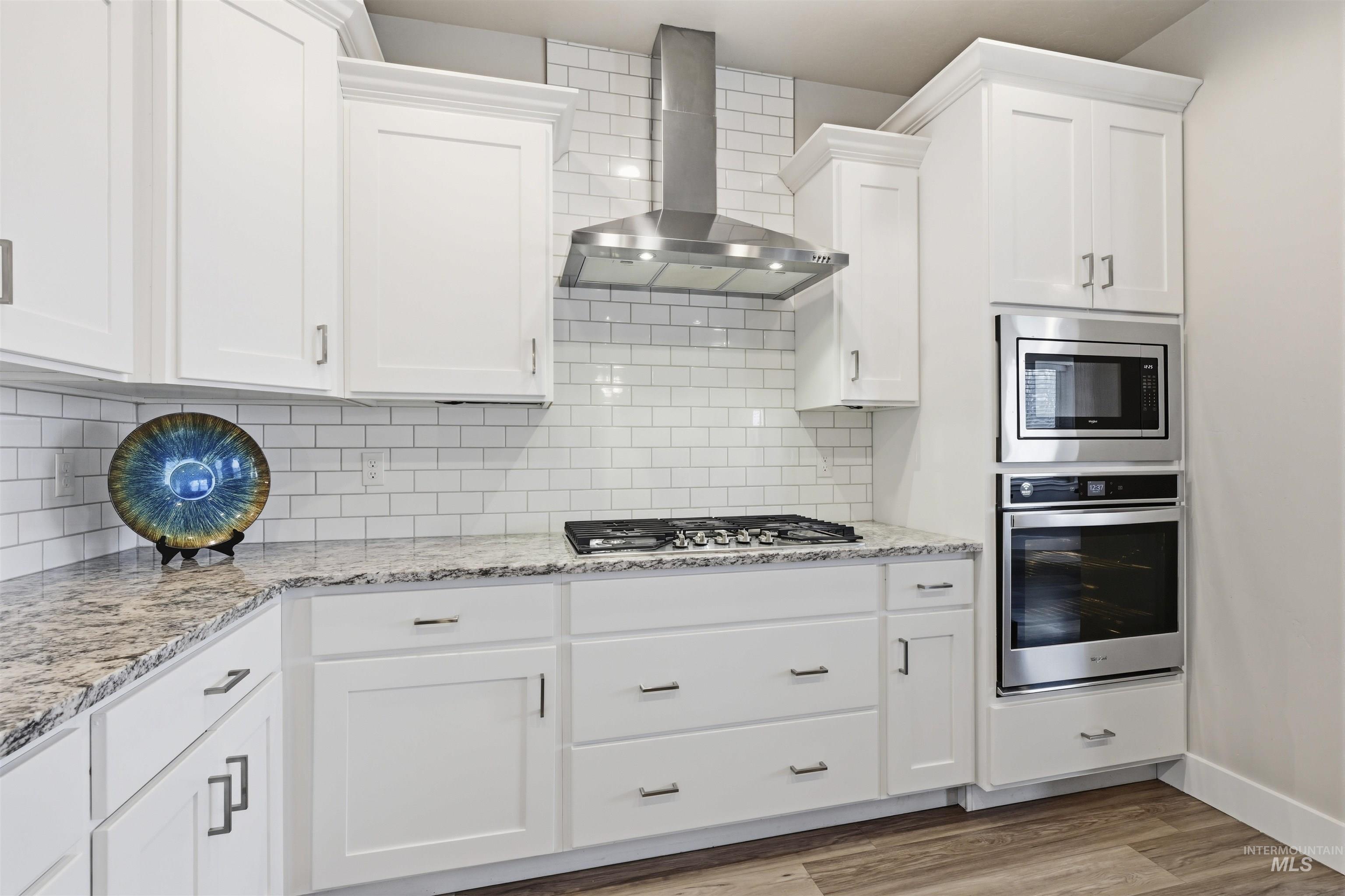 2229 East Grayson Street Meridian, ID 83642 - Photo 13 of 40 Kitchen with wall chimney range hood, stainless steel appliances, light stone countertops, and white cabinets