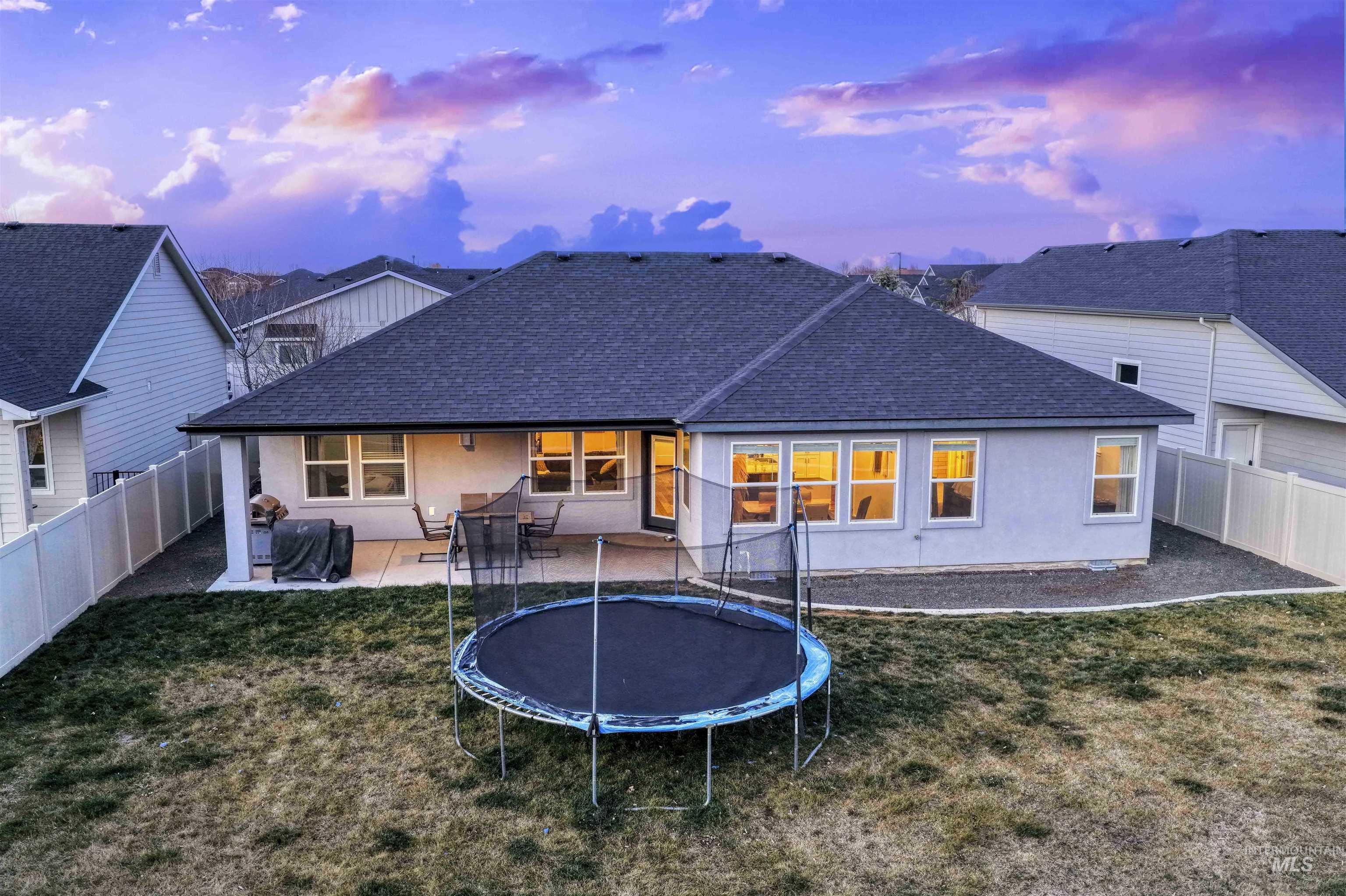 2229 East Grayson Street Meridian, ID 83642 - Photo 37 of 40 Back of house at dusk featuring roof with shingles, a patio, a fenced backyard, stucco siding, and a trampoline