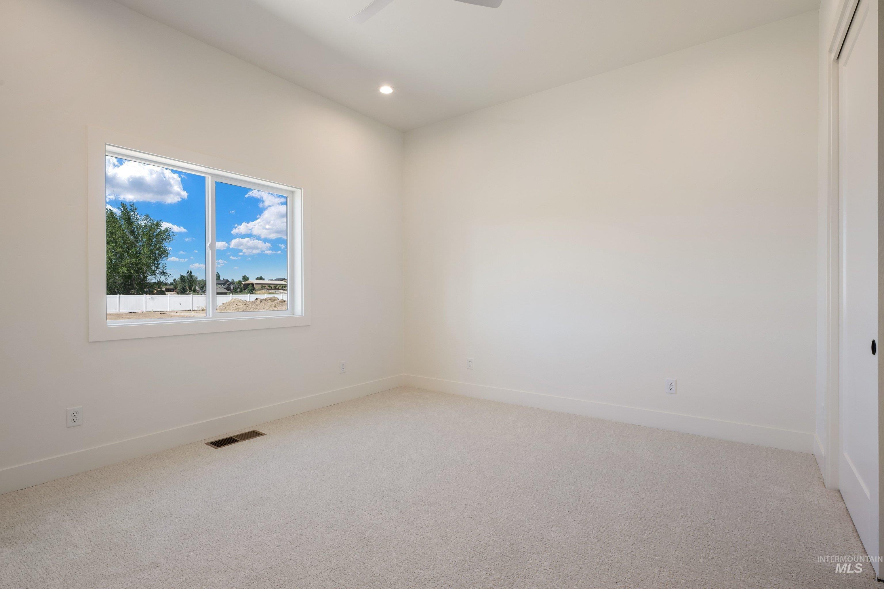 24821 Ardmore Court Caldwell, ID 83607 - Photo 34 of 43 Spacious room with plush light-toned carpeting, ample natural light from a large window, a ceiling fan, recessed lighting, and a white interior door