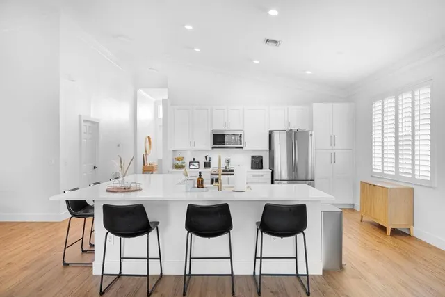 a kitchen with stainless steel appliances kitchen island granite countertop a dining table chairs and a refrigerator