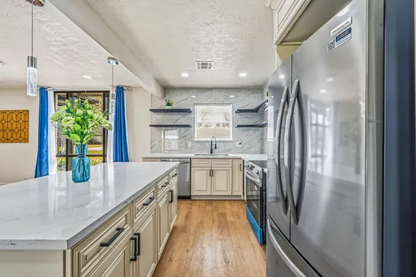 a kitchen with stainless steel appliances granite countertop a refrigerator a sink dishwasher a stove and white countertops with wooden floor