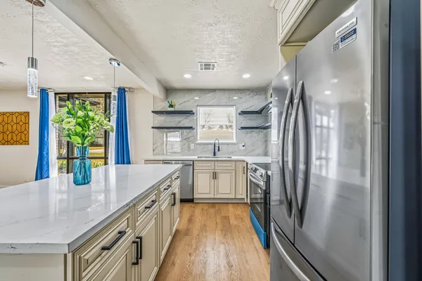 a kitchen with stainless steel appliances granite countertop a refrigerator a sink dishwasher a stove and white countertops with wooden floor