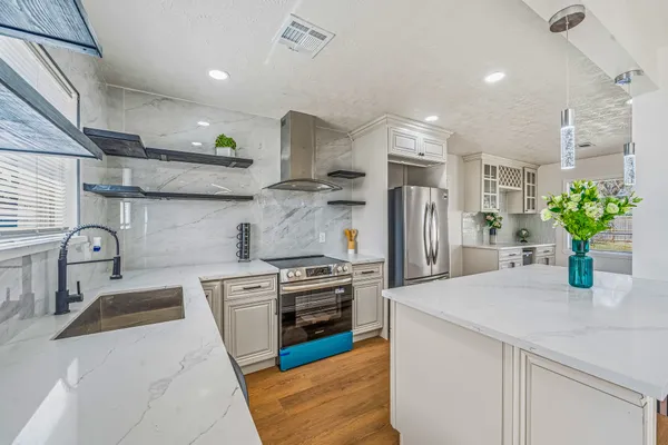 a kitchen with stainless steel appliances granite countertop a sink a stove a refrigerator a window with white cabinets and wooden floor