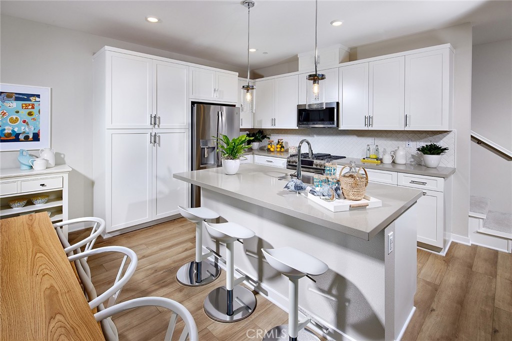 a kitchen with stainless steel appliances granite countertop a sink a stove a refrigerator and white cabinets with wooden floor