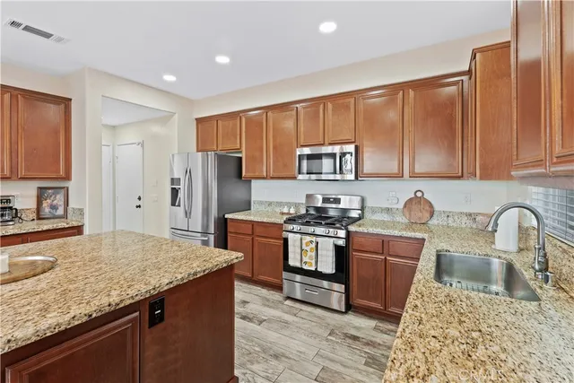 a kitchen with stainless steel appliances granite countertop a stove top oven a sink dishwasher a refrigerator and cabinets with wooden floor