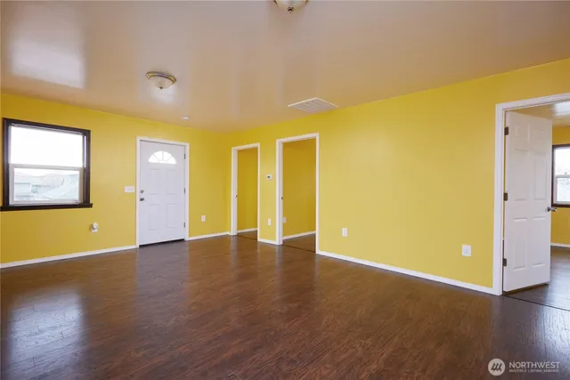 a view of an empty room with wooden floor and a window