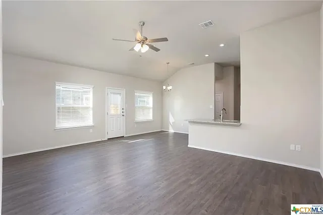 an empty room with wooden floor ceiling fan and windows