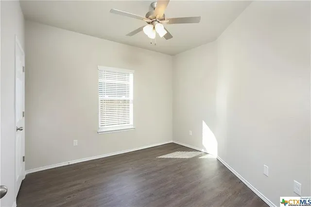 an empty room with wooden floor ceiling fan and windows