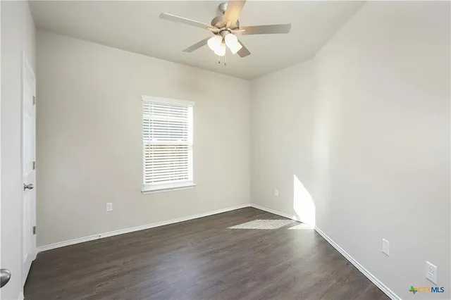 an empty room with wooden floor chandelier fan and windows